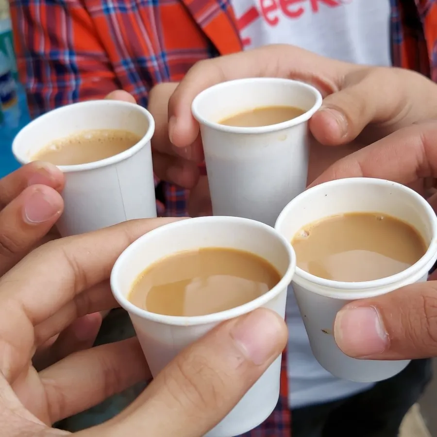 Four hands holding paper cups of cutting chai — a ritual in both Mumbai and Ahmedabad